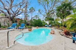 A swimming pool with a metal ladder, surrounded by blue lounge chairs and potted plants.