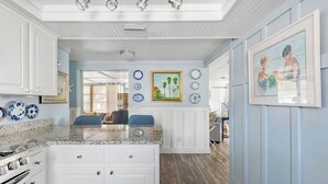 A kitchen with white cabinets, a granite countertop, and a dining area with blue chairs. - Coastal Retreat with Private Pool on Manasota Key (Englewood)