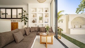 A modern living room with a sectional sofa, a round wooden table, and a white shelving unit with decorative items. - Villa Nikki Uluwatu (Uluwatu)