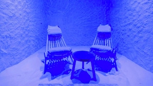 Interior cubierto de nieve con dos sillas y una mesa pequeña, evocando un ambiente invernal.