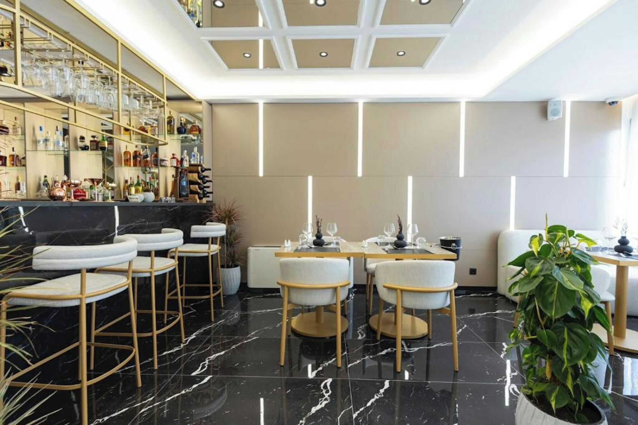 A modern bar area with a marble floor, bar stools, and a glass display of bottles.