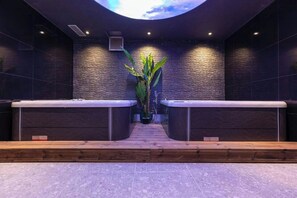 Een wellnessruimte met twee houten banken, een centrale plant en een stenen muur.