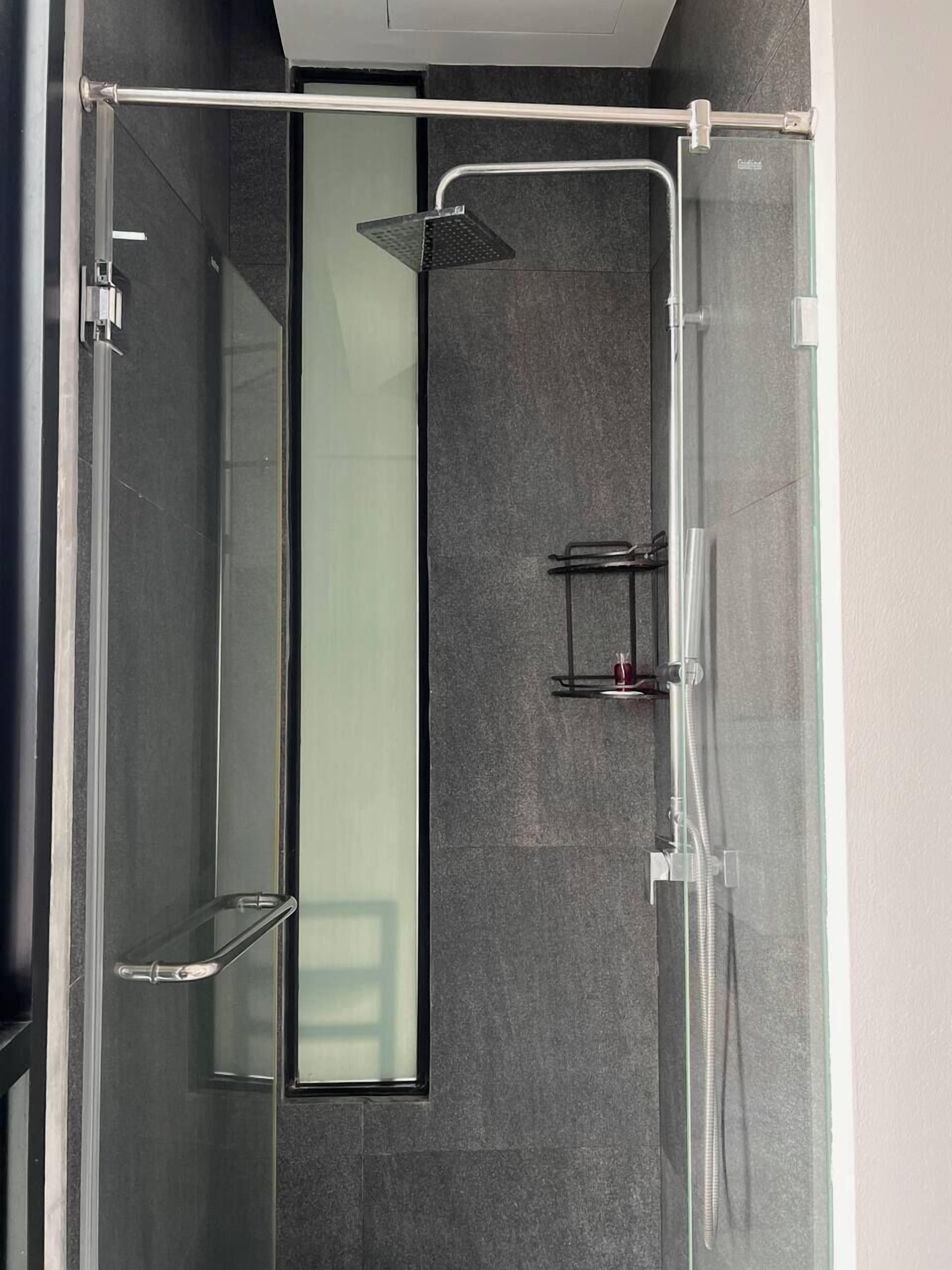 Une cabine de douche moderne dotée d’une porte en verre, d’un pommeau de douche à main et d’un robinet mural.