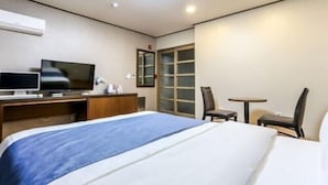 Una habitación de hotel con una cama, un escritorio con computadora, televisor, una silla y una mesita.