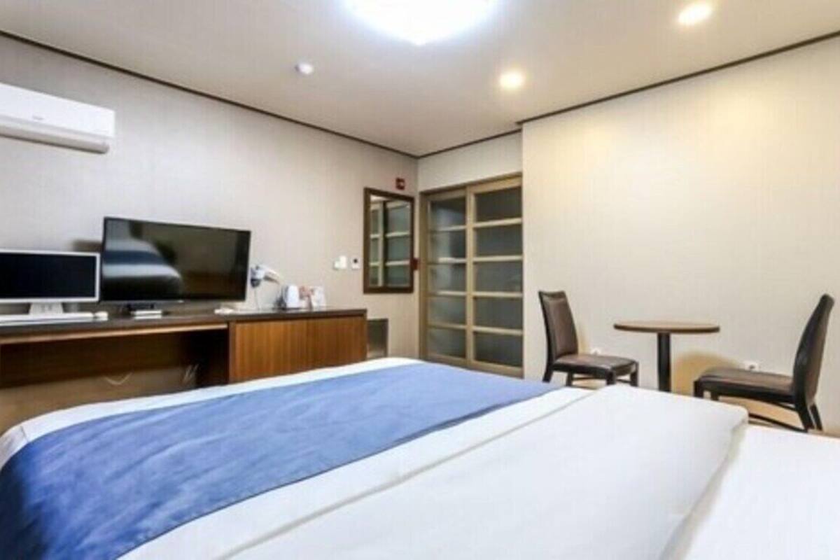 Ein Hotelzimmer mit einem Bett, einem Schreibtisch mit Computer, einem Fernseher, einem Sessel und einem kleinen Tisch.