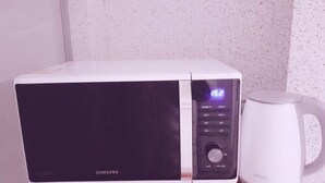 Un microondas con pantalla digital y una cafetera sobre una superficie de madera.