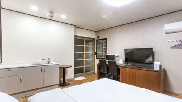 Una habitación de hotel con cama, escritorio, silla, televisor, armario y ventana.