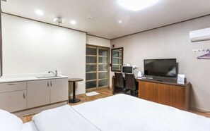 Una habitación de hotel con cama, escritorio, silla, televisor, armario y ventana.
