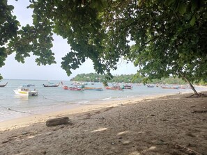 Une plage avec des bateaux ancrés dans l’eau, un rivage sablonneux et un arbre qui offre de l’ombre.