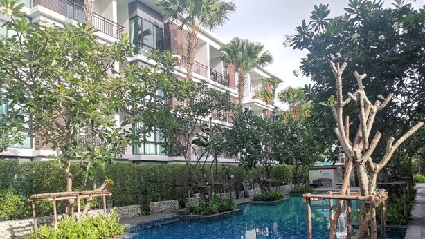 Una piscina envoltada d'arbres i un edifici d'àmbit elevat amb balcons.