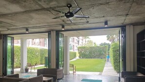 Zona interior amb seients, un ventilador de sostre i vista a un verd camp de gespa i edificis.