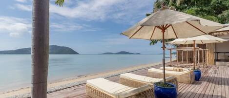 A wooden deck with lounge chairs and umbrellas overlooking a calm sea and distant islands.