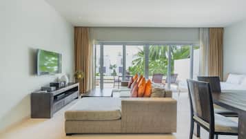 A modern living room with a sofa, a TV, a dining table, and a view of the outdoors.