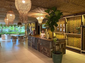 A reception area with a wooden counter, wicker furniture, and hanging light fixtures. - NEW Serenity Tropical 2 Bed Condo On Beachfront (Rawai)