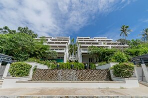 A modern hotel with a symmetrical facade, multiple balconies, and lush greenery surrounding the property. - NEW Serenity Tropical 2 Bed Condo On Beachfront (Rawai)