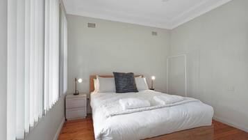 A bedroom with a bed, bedside tables, a nightstand, a window with blinds, and a door.