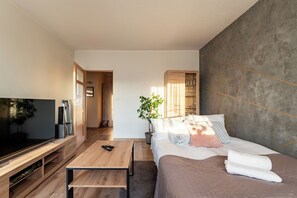 Moderni hotellihuone, jossa on sänky, televisio, puinen pöytä ja kasvi.