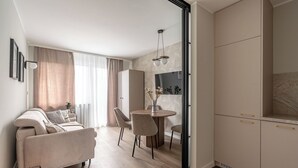 A modern living room with a sofa, dining table, chairs, and a kitchen area with cabinets. - Przymorze Kaszmirowy Apartment (Gdańsk)