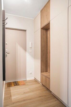 Un couloir avec une porte, un porte-manteau, un interrupteur et une armoire en bois.