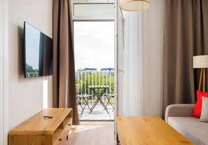 A modern hotel room with a TV, wooden furniture, a balcony with outdoor seating, and a view of the city. - Warszawa Rakowiec Deluxe Apartment (Warszawa)