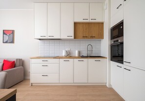 A modern kitchen with white cabinets, a wooden countertop, and a built-in oven. - Warszawa Rakowiec Deluxe Apartment (Warszawa)