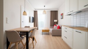 A modern kitchen with white cabinets, a wooden countertop, and a dining area with a table and chairs. - Warszawa Rakowiec Deluxe Apartment (Warszawa)