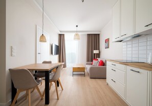 A modern kitchen with white cabinets, a wooden countertop, and a dining area with a table and chairs. - Warszawa Rakowiec Deluxe Apartment (Warszawa)