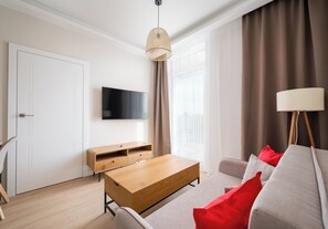 A modern living room with a wooden coffee table, a sofa with red cushions, a TV mounted on the wall, and a large window with curtains. - Warszawa Rakowiec Deluxe Apartment (Warszawa)