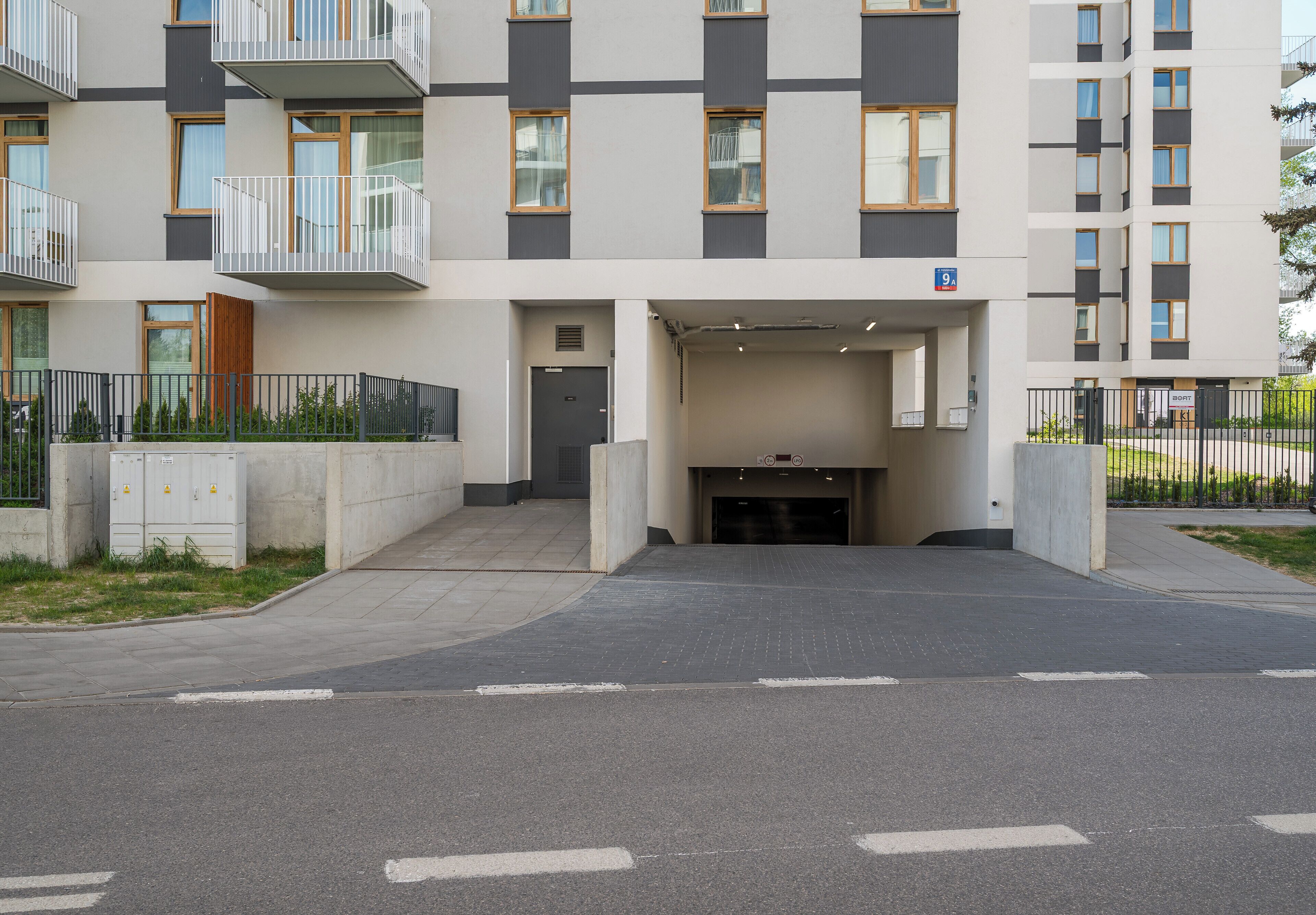 A multi-story residential building with balconies, a garage entrance, and a gated driveway.
