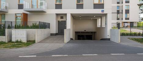 A multi-story residential building with balconies, a garage entrance, and a gated driveway.