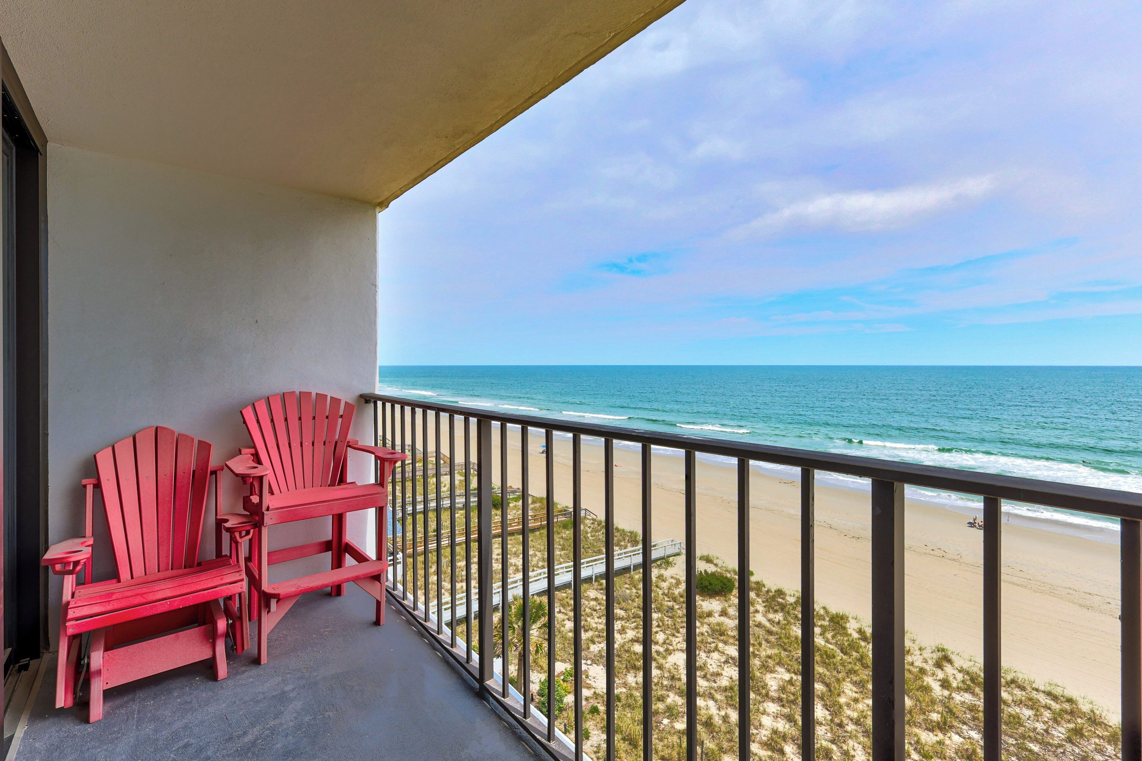 A balcony with red Adirondack chairs overlooking a beach and ocean.