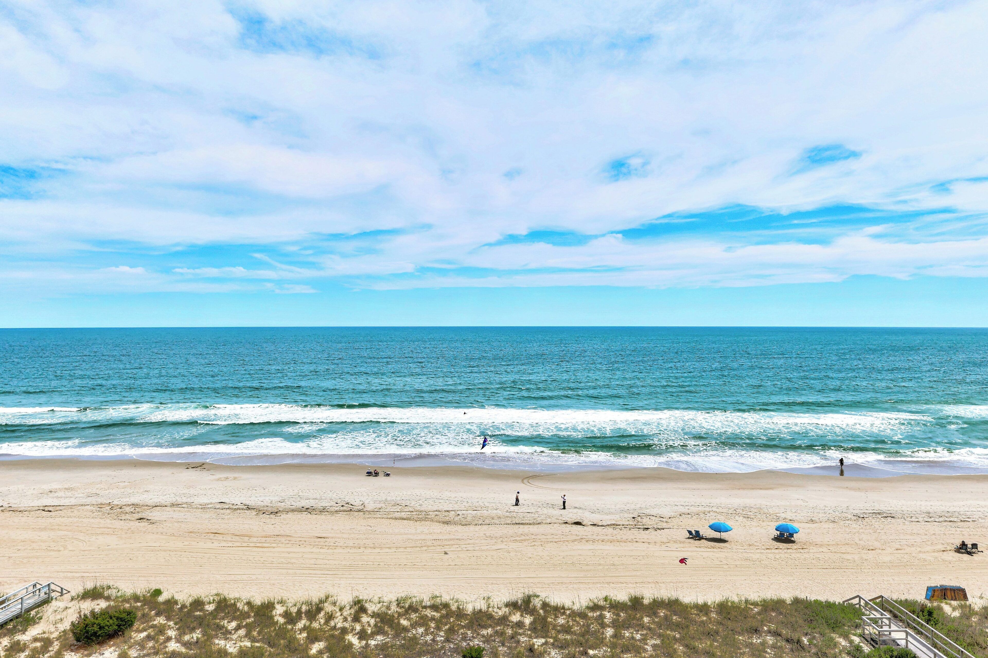 Een strand met heldere lucht, golven in de oceaan en enkele mensen en parasols.
