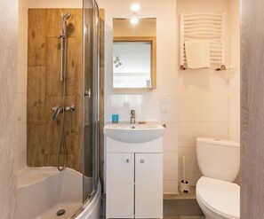 A bathroom with a glass-enclosed shower, a white sink, a toilet, and a wooden panel wall. - Gdynia Morska Horizon Studio (Gdynia)
