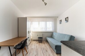 A small, modern room with a wooden desk, a black chair, a light blue sofa, and a radiator.