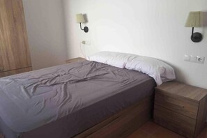 Een slaapkamer met een bed, nachtkastje, wandlamp en een houten garderobe.
