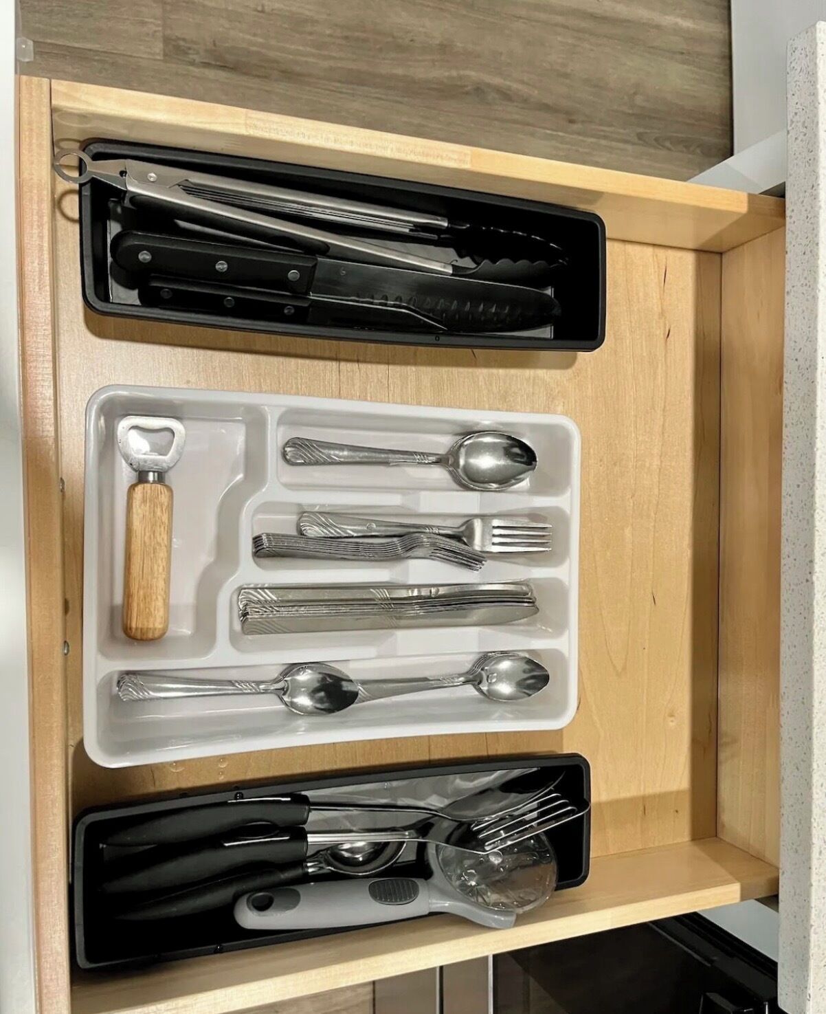 A drawer with neatly organized kitchen utensils, including knives, spoons, forks, and a whisk.