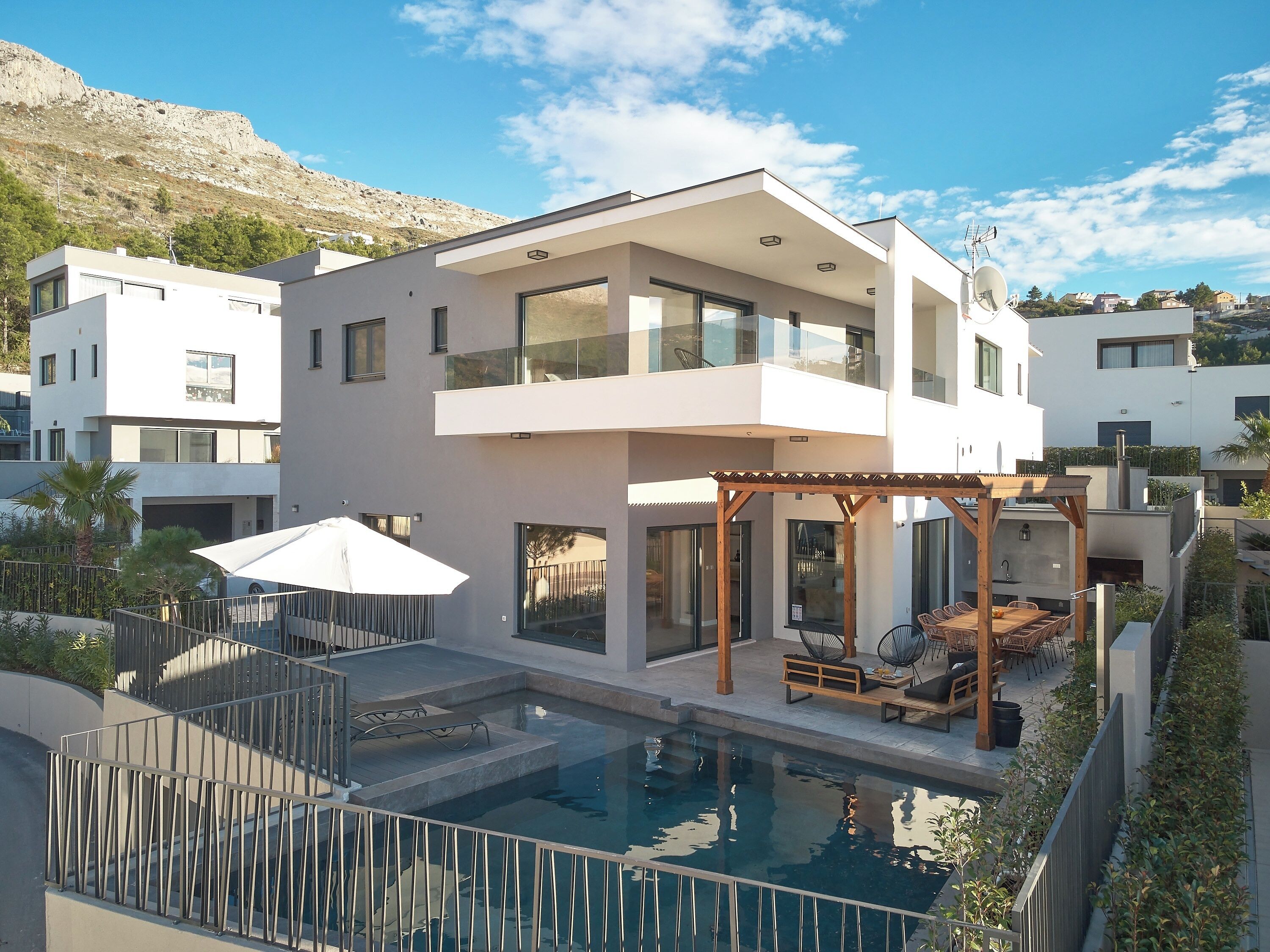 Une maison moderne à deux étages, dotée d’une piscine, d’un espace extérieur aménagé et offrant une vue sur le quartier environnant.