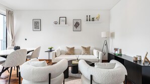 Ein modernes Wohnzimmer mit einem weißen Sofa, zwei Sesseln, einem Couchtisch und einer Anrichte.