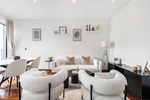 Ein modernes Wohnzimmer mit einem weißen Sofa, zwei Sesseln, einem Couchtisch und einer Anrichte.