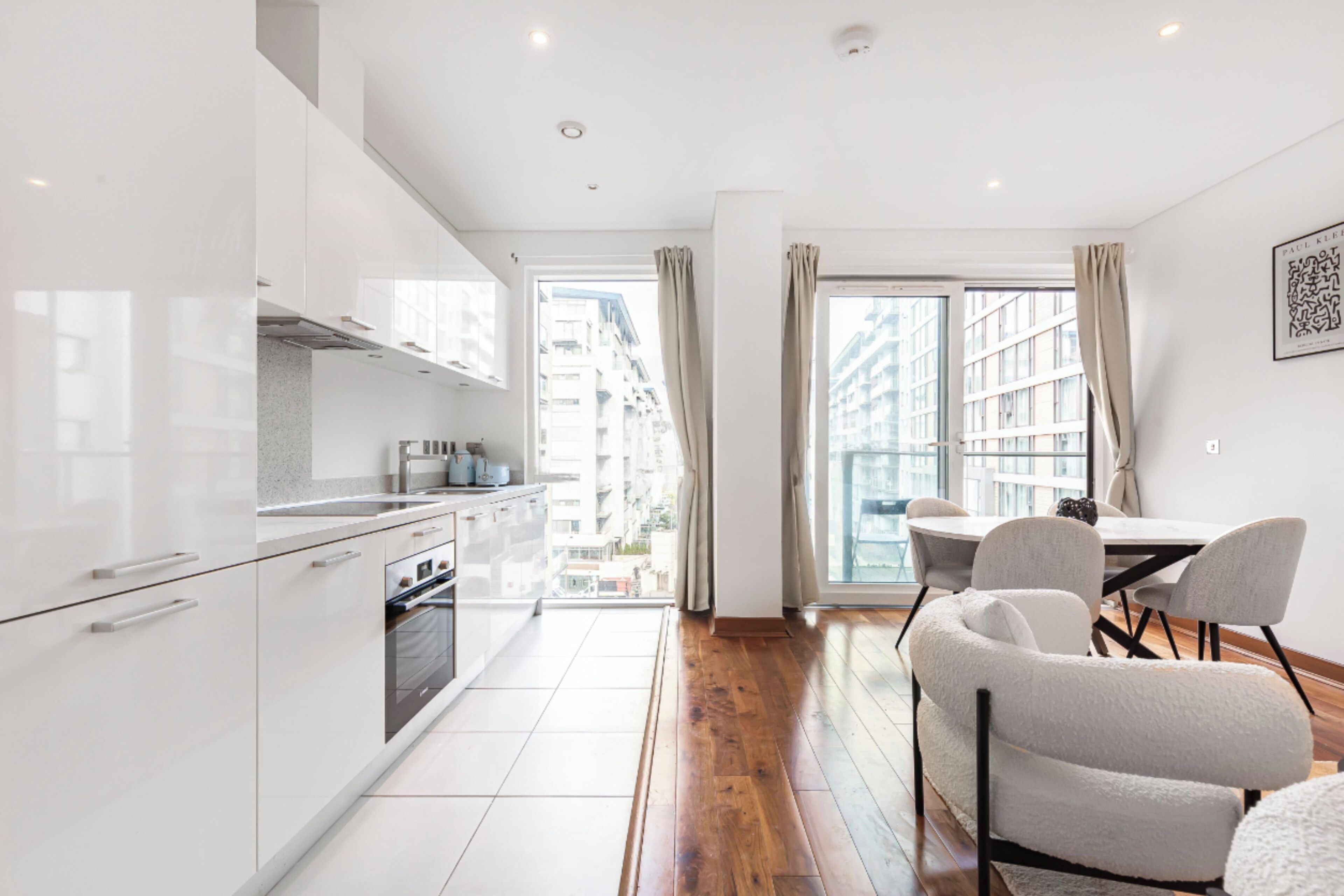 A modern kitchen with white cabinets, a dining area with a table and chairs, and a large window with curtains.
