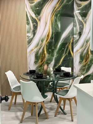 Un comedor con una mesa redonda de vidrio, sillas blancas y una pared de mármol con vetas doradas.
