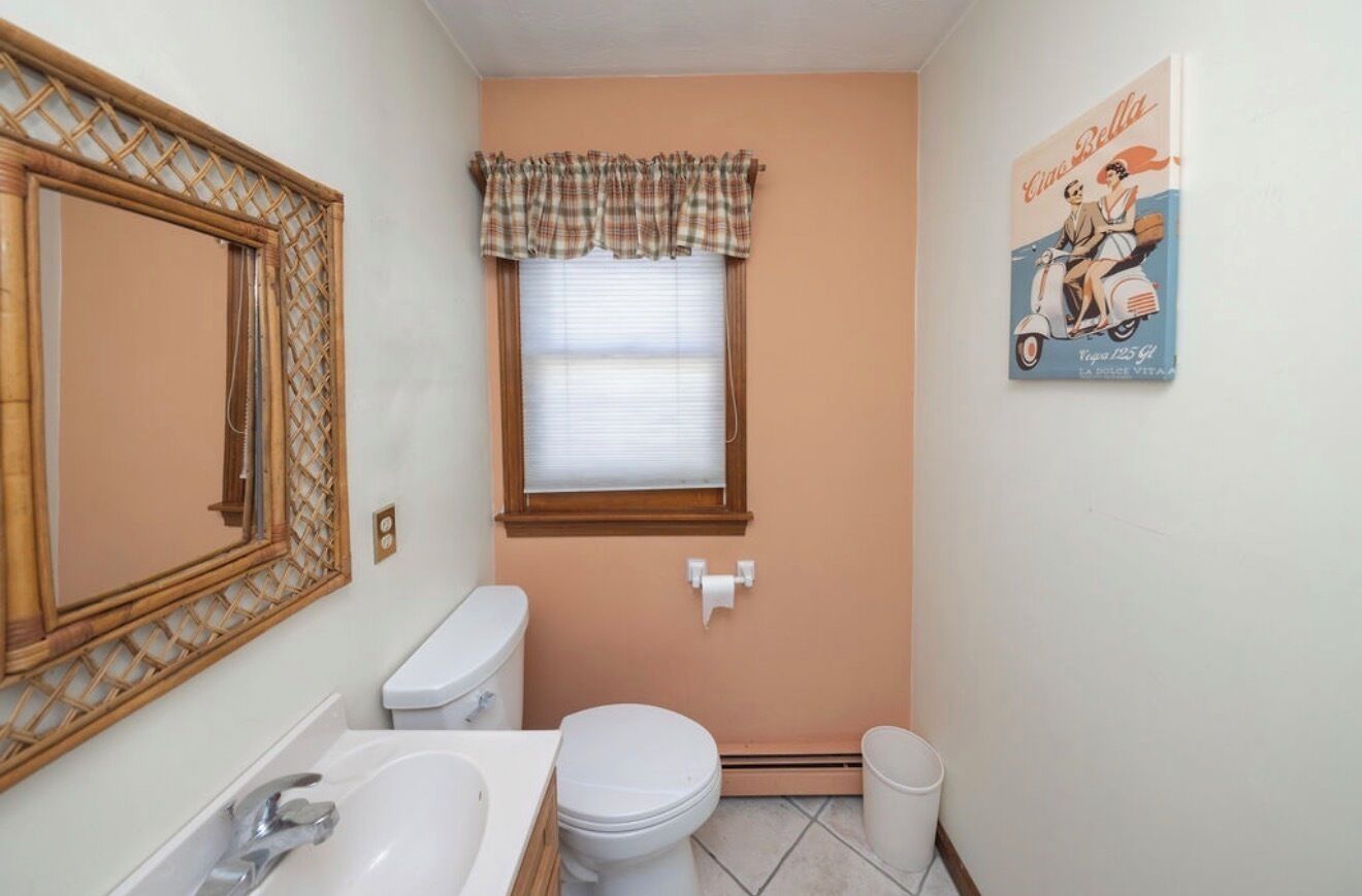 Een badkamer met toilet, wastafel en raam met ruitgordijn.