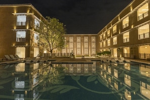 Un pati d'hotel amb piscina, múltiples balcons i un arbre gran.