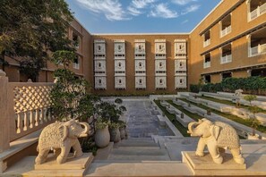 Um pátio com uma escadaria central, uma estátua decorativa de elefante e um edifício com várias varandas.