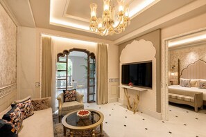 Uma sala de estar luxuosa com um lustre, um conjunto de sofás, uma televisão e um espelho decorativo.