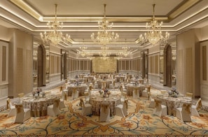 Un gran espai per a banquets amb diverses taules rodones, penjants de cristall i decoracions murals ornamentals.