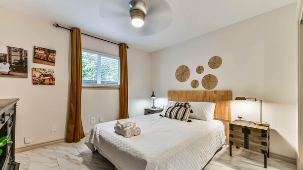 Ein ordentlich eingerichtetes Schlafzimmer mit Bett, Nachttisch, Lampe und Wandbildern.