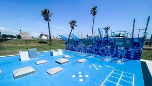 Ein blauer Outdoor-Fitnessbereich mit Trainingsgeräten, Palmen und blauem Himmel.