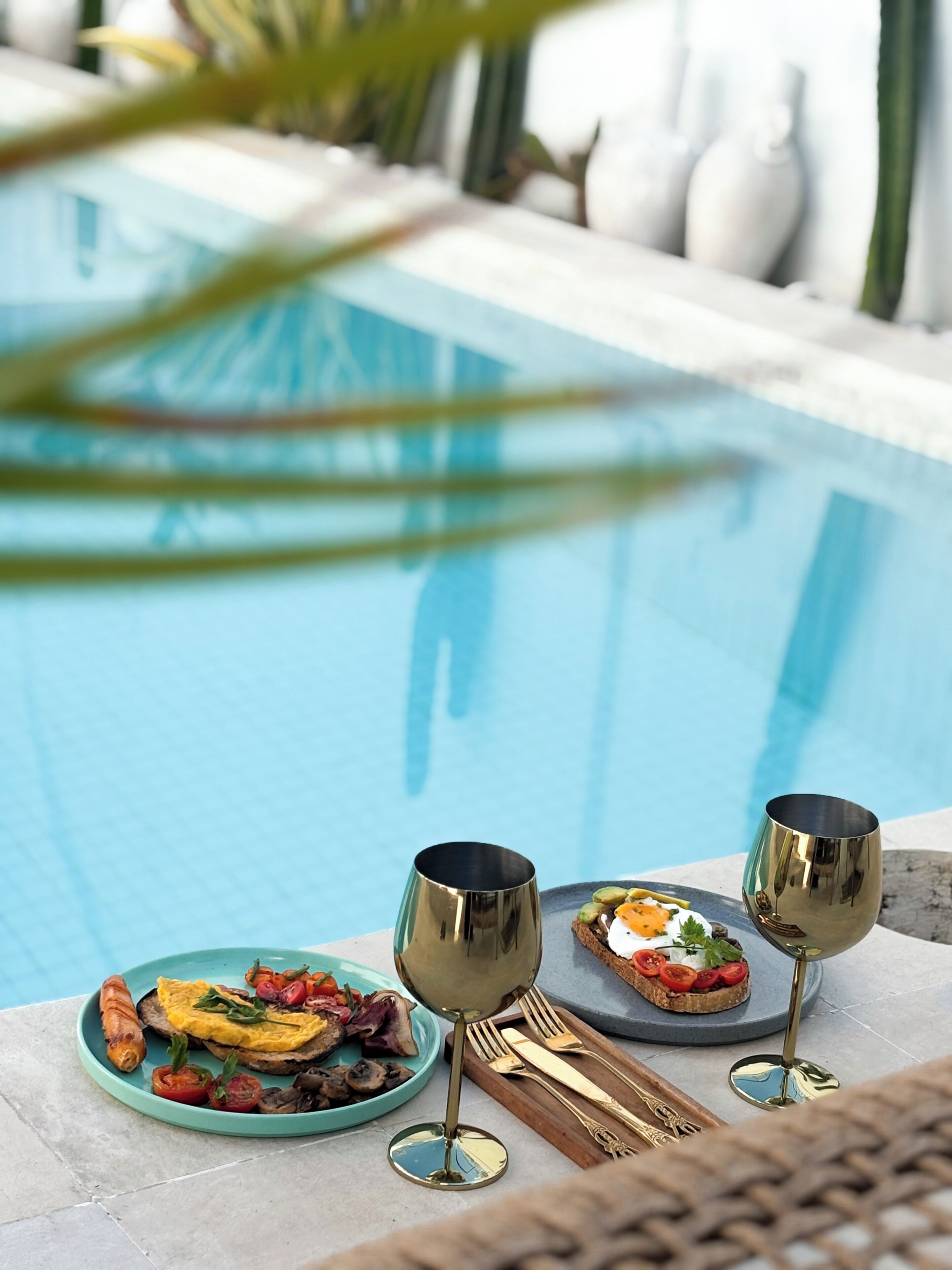 A poolside dining setup with a plate of food, two glasses, and cutlery.