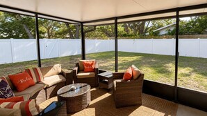 Un patio couvert aménagé avec des meubles en osier, une table en verre et une vue sur un jardin clos.